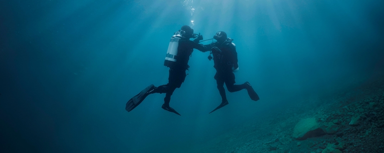 Scéna pod vodou: potápěč podporuje druhého potápěče, který má problémy s přívodem vzduchu.